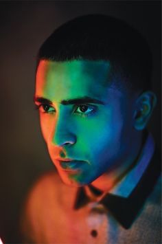 a young man with blue and green light on his face, looking at the camera