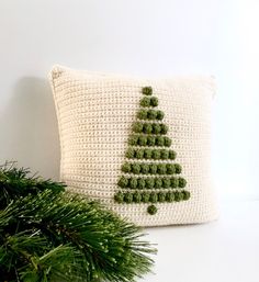 a crocheted christmas tree pillow sitting on top of a table next to a pine branch