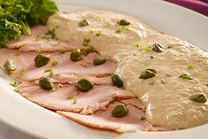 a white plate topped with meat covered in sauce and garnished with green vegetables