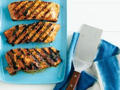 three pieces of grilled fish on a blue plate with a spatula next to it