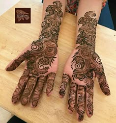 two hands with henna tattoos on them sitting on top of a wooden table next to each other