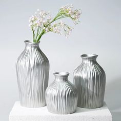 three silver vases sitting on top of a white block