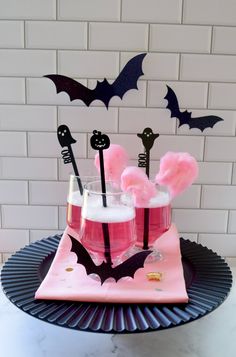 two glasses filled with liquid and bats on top of a pink table cloth covered plate