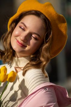 a young woman wearing a yellow hat and holding a flower in her right hand while smiling