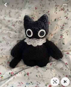 a black stuffed animal with big eyes and lace collar on it's neck sitting on a bed