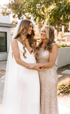 two women standing next to each other in front of a tree wearing dresses and veils