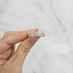 a woman's hand holding a diamond ring in front of a white marble background