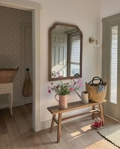 a wooden bench sitting under a mirror next to a vase with flowers on top of it