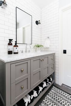 a bathroom with white brick walls and gray vanity, black and white patterned rugs