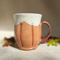 a coffee cup sitting on top of a table next to leaves and a white cloth