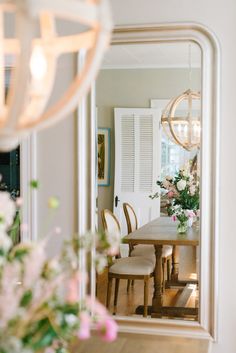 a dining room table with chairs and flowers in the vases on the far wall