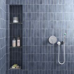 a blue tiled bathroom with shelves and shower head