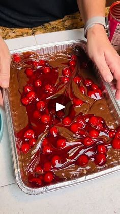 someone is decorating a chocolate cake with cherries on the top and bottom layer