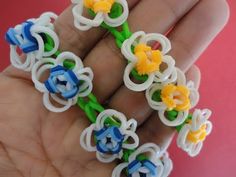 a hand is holding some colorful plastic beads on it's fingers and there are flowers in the middle