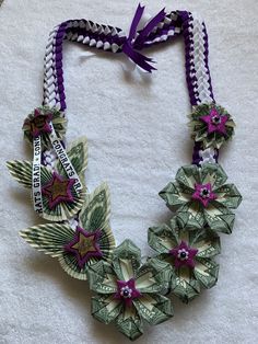 a necklace made out of dollar bills with purple flowers and ribbons hanging from it's sides