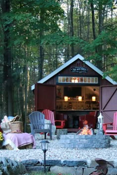 a fire pit in the middle of a forest with chairs around it and a shed behind it