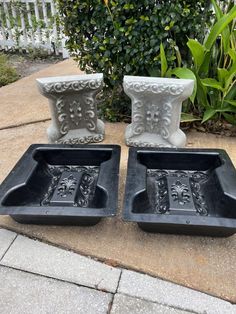 two black and white planters sitting on top of a cement slab next to each other