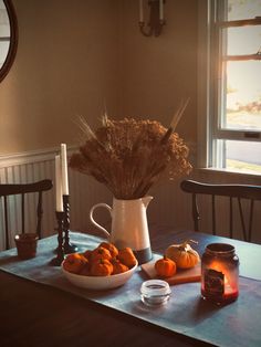 the table is set with pumpkins and dried flowers in a white pitcher on it