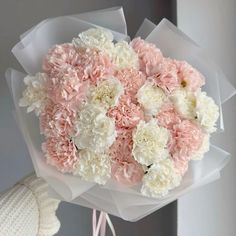 a bouquet of pink and white carnations is held by someone's hand