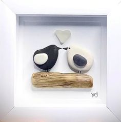 two birds sitting on top of a piece of driftwood in a white box frame