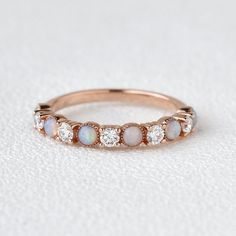 a rose gold ring with white opal and diamonds on the side, sitting on a white surface