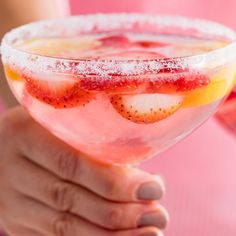 a hand holding a glass filled with liquid and fruit on the rim, topped with powdered sugar