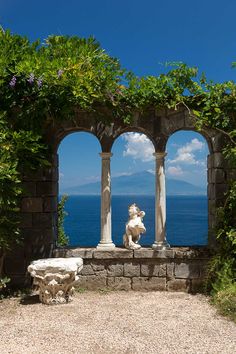 a stone bench sitting in front of an arch covered with vines and flowers next to the ocean