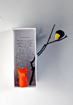 an orange cat sitting in a box next to a branch with a bird on it