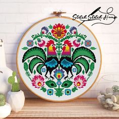 a cross stitch pattern with roosters and flowers on the front, in a wooden frame