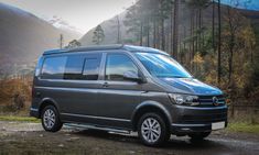 a grey van parked on the side of a road in front of trees and mountains