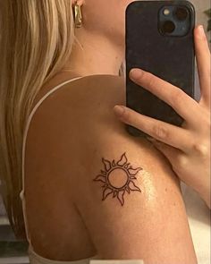 a woman with a sun tattoo on her arm holding a cell phone up to her face