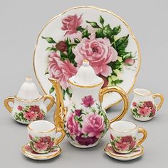 a porcelain tea set with pink flowers and gold trimmings on the front, sitting next to two matching cups and saucers