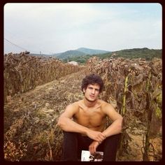 a shirtless man sitting in the middle of a corn field with his hands on his knees