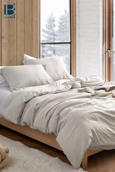 a white bed sitting in a bedroom next to a wooden headboard and large windows