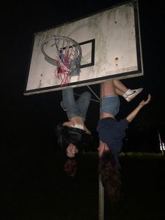 two girls are playing basketball on a pole in the dark, one is upside down