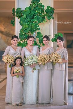 a group of women standing next to each other in dresses and holding bouquets with greenery behind them