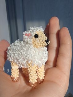 a hand holding a tiny toy sheep made out of bead and glass seed beads