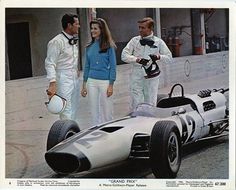 two men and a woman standing next to a race car