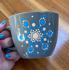 a hand holding a gray and blue coffee cup on a wooden table with white dots