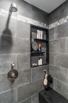 a gray tiled bathroom with shelves above the sink and soap dispenser on the wall