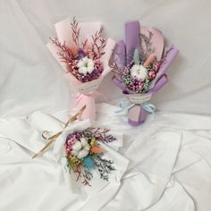 three bouquets of flowers are sitting on a white cloth covered bed sheet, one is purple and the other is pink