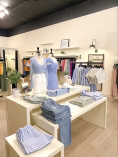 clothes on display in a clothing store with wooden flooring and white tables topped with shirts