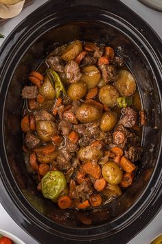 a crock pot filled with meat and vegetables on top of a white countertop