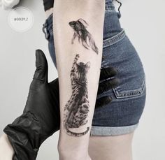 a woman's arm with a cat and fish tattoo on the left side of her arm