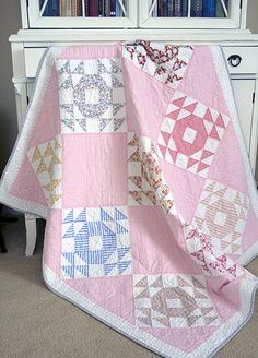 a pink and white quilt sitting on top of a bed next to a book shelf