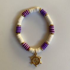 a white bracelet with purple and gold beaded beads, a small charm on it