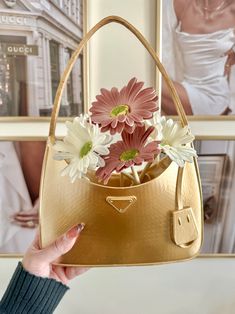 a woman holding a gold purse with flowers in the front and side pockets on both sides