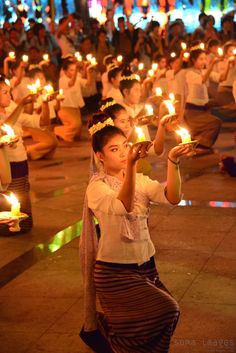 a woman holding candles in her hands while sitting on the ground with others behind her