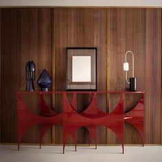 a red console table in front of a wood paneled wall with a mirror on it