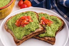 two pieces of toast with guacamole and tomatoes on them sitting on a white plate